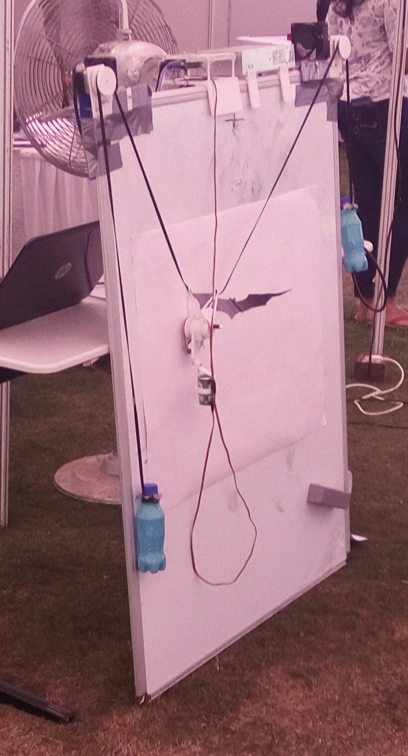 Bono halfway through the Batman logo on paper taped to the whiteboard, counterweight bottles hanging on both cords