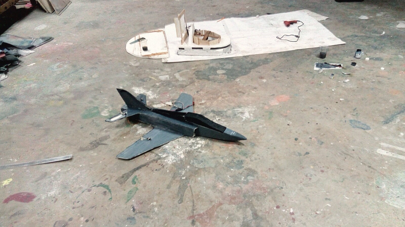 A grey-painted foam fighter jet on the workshop floor, February 2016, with a half-built hovercraft in the background