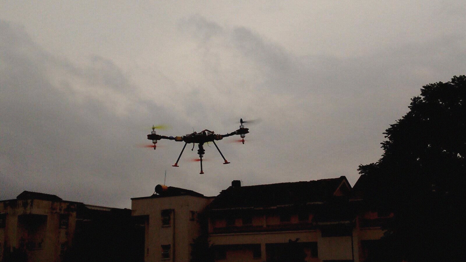 The quadcopter silhouetted against a monsoon sky above the hostel rooftops