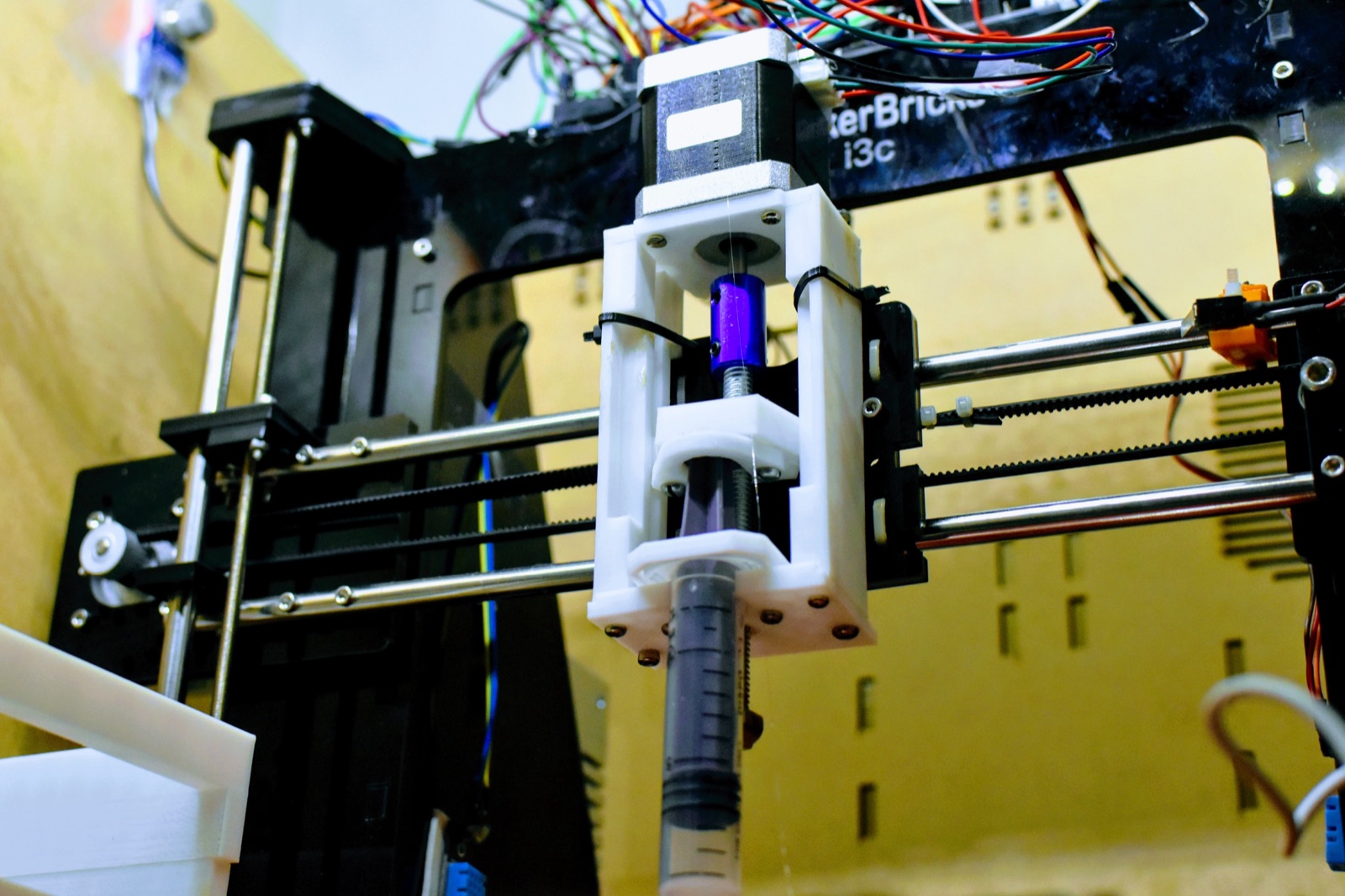 The custom syringe extruder: a NEMA stepper driving a leadscrew through a 3D-printed carriage that presses a standard syringe