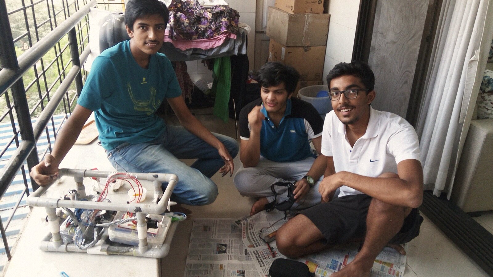 The team on a balcony floor around the frame, FPV goggles out, newspaper spread under the messy work